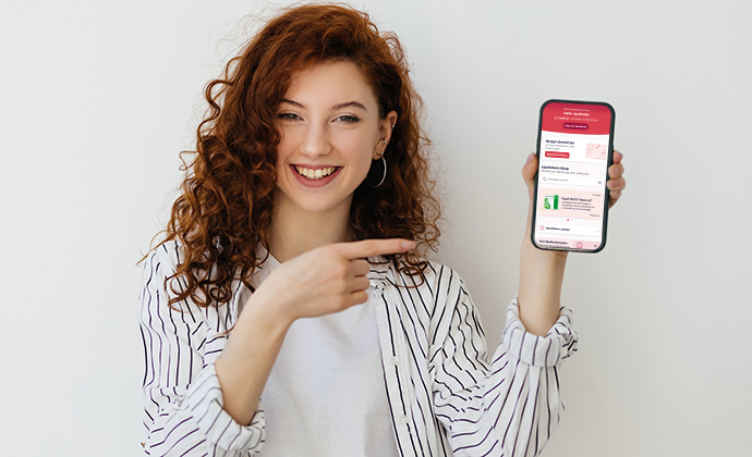 Portrait of an attractive happy young woman with long curly red hair standing isolated over white background, showing blank sreen mobile phone